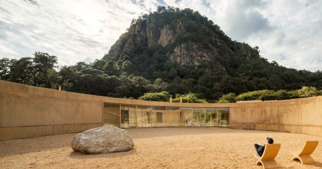Vista exterior de una casa de tonos terrosos con diseño curvo, integrada en un valle montañoso mexicano.